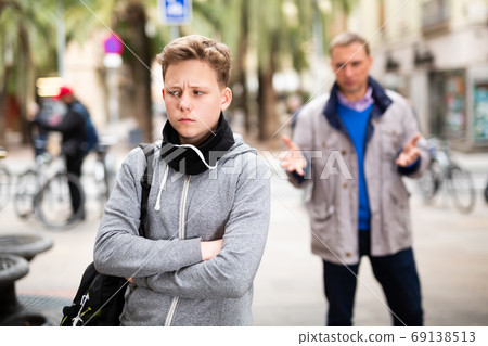 Frowning teenager listening to reprimanding from father Frowning teenager listening to reprimanding from father 69138513