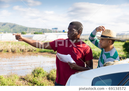 Farmers with papers talking near car on farm field 69138572