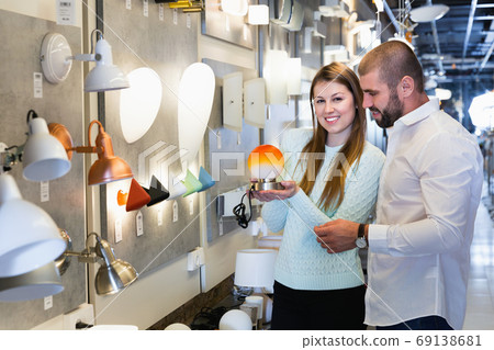Smiling couple customers choosing bedside lamp in furniture store Smiling couple customers choosing bedside lamp in furniture store 69138681