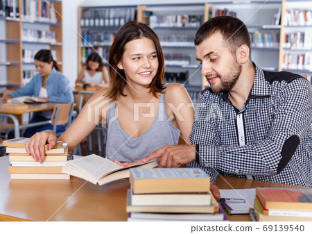 Young people reading and making notes while preparing for exam in college library Young people reading and making notes while preparing for exam in college library 69139540