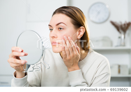Smiling female is looking on her skin in the mirror 69139602