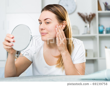 Cheerful woman is concentrared looking on her face in the mirror 69139758