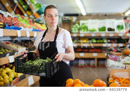 Young female seller standing with box of green beans in shop 69139779