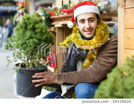 Young man choosing small Christmas tree at Christmas market Young man choosing small Christmas tree at Christmas market 69139826