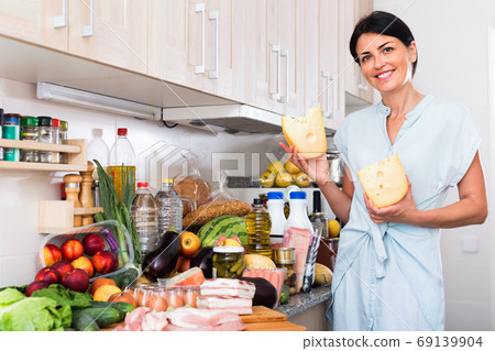 Female is posing with cheese and milk in time cooking on the kitchen at home. Female is posing with cheese and milk in time cooking on the kitchen at home. 69139904