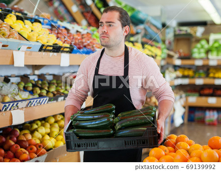 Young male seller offering green zucchini from tray in store Young male seller offering green zucchini from tray in store 69139992