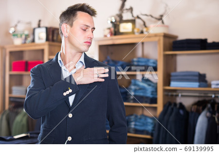 Male customer is trying on new dark blue jacket Male customer is trying on new dark blue jacket 69139995