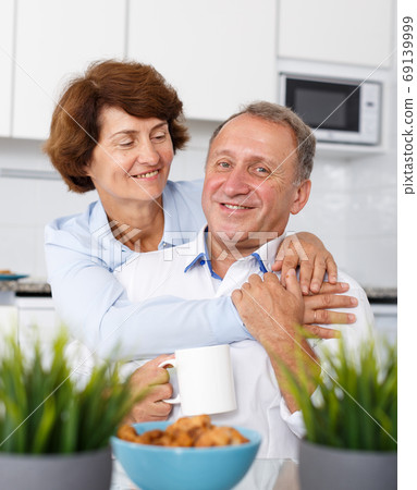 Mature family couple hugging at kitchen table during drinking tea Mature family couple hugging at kitchen table during drinking tea 69139999