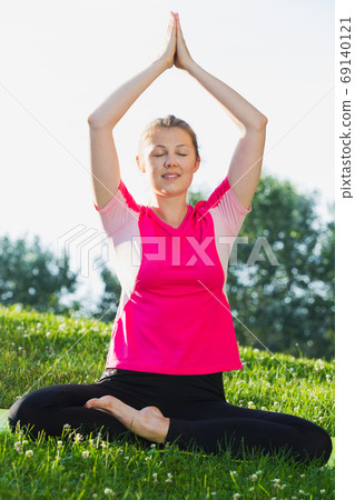 Female in pink T-shirt is sitting and practising meditation Female in pink T-shirt is sitting and practising meditation 69140121