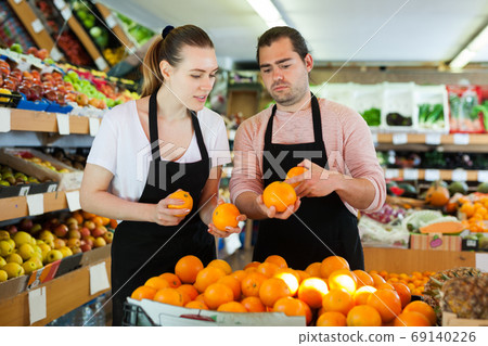 Male and woman standing and holding fresh oranges in fruit store Male and woman standing and holding fresh oranges in fruit store 69140226