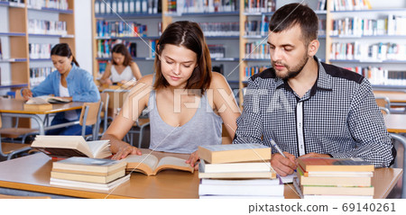 Young people reading and making notes while preparing for exam in college library Young people reading and making notes while preparing for exam in college library 69140261
