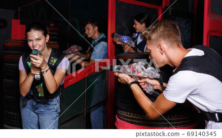 Portrait of friends standing with laser guns during laser tag game in dark room Portrait of friends standing with laser guns during laser tag game in dark room 69140345