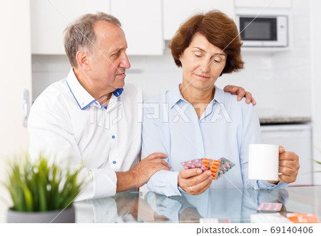 Unhappy mature couple sittimg at kitchen table and taking drugs in home Unhappy mature couple sittimg at kitchen table and taking drugs in home 69140406