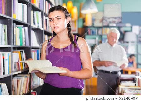 Teenage girl is choosing textbook for preparing to exam in bookstore. Teenage girl is choosing textbook for preparing to exam in bookstore. 69140407