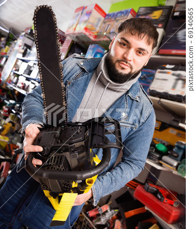 Positive consumer chooses chainsaw in a tool store Positive consumer chooses chainsaw in a tool store 69140665