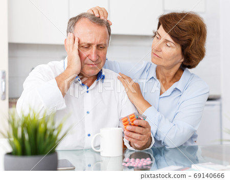 Sad mature family couple with medicine sitting at kitchen table Sad mature family couple with medicine sitting at kitchen table 69140666
