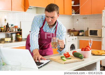 Man using laptop during cooking Man using laptop during cooking 69141026