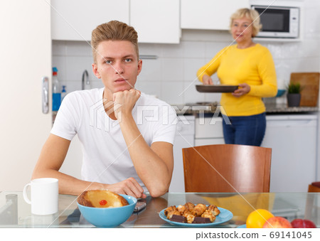 Woman cooking breakfast to her adult son Woman cooking breakfast to her adult son 69141045