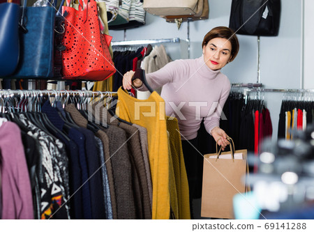 Female shopper examining warm sweaters in women’s cloths shop 69141288