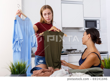 Smiling young women friends chatting and looking at clothes together Smiling young women friends chatting and looking at clothes together 69141846