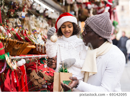 Man and girl with toy choosing decorations at Christmas market Man and girl with toy choosing decorations at Christmas market 69142095