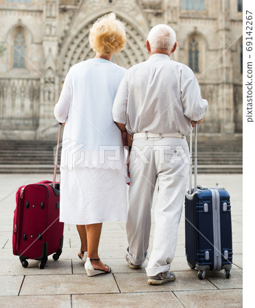 Senior tourists strolling with suitcases 69142267