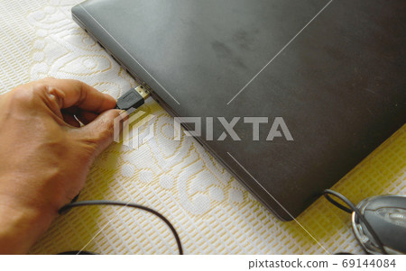 Human hand connecting Computer mouse connection cable plug-in the laptop keyboard.  69144084