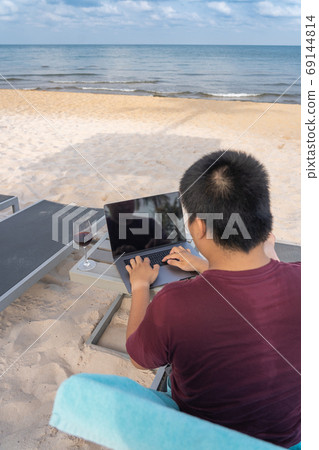 Asian man working with laptop by the beach Asian man working with laptop by the beach 69144814