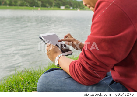 Man sitting in the park, using tablet Man sitting in the park, using tablet 69145270
