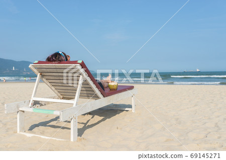 Rear view of woman lying on sandy summer beach chair Rear view of woman lying on sandy summer beach chair 69145271