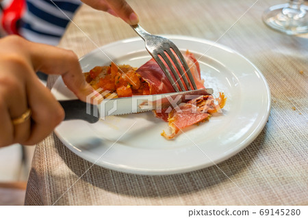 Human hand cutting cured meat slice on white plate 69145280