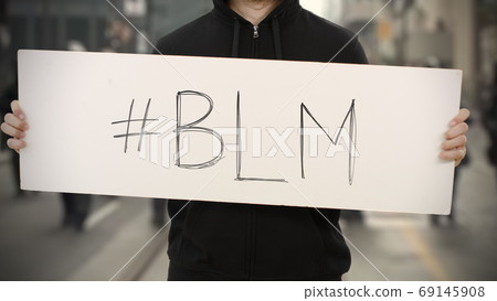 Activist wearing dark clothes holds a placard with BLM or Black Lives Matter hashtag Activist wearing dark clothes holds a placard with BLM or Black Lives Matter hashtag 69145908