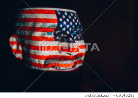 Adult man with USA flag on his face in the dark. Adult man with USA flag on his face in the dark. 69146282