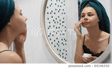 A shot of young beautiful woman applying lotion to her face A shot of young beautiful woman applying lotion to her face 69146350