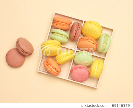 wooden box and baked multi-colored macarons cookies on a beige b 69146579