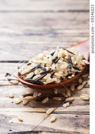 Raw wild rice in a wooden spoon. Raw rice grits on a wooden background. Copy space. 69146823