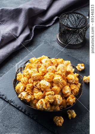 Popcorn in caramel glaze in a plate on a dark concrete table. Copy space. 69146833