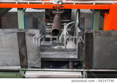 Band saw for industrial high speed cutting metal pipe and using coolant. Precision equipment on manufacture factory line of heavy industry indoors. Hack sawing machine working to cutting metal. Band saw for industrial high speed cutting metal pipe and using coolant. Precision equipment on manufacture factory line of heavy industry indoors. Hack sawing machine working to cutting metal. 69147746