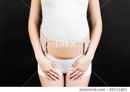 Close up of pregnant woman with supporting bandage against backache at black background with copy space. Orthopedic abdominal support belt concept Close up of pregnant woman with supporting bandage against backache at black background with copy space. Orthopedic abdominal support belt concept 69151863