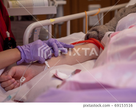 A nurse inserting a canula into a patient's arm 69153516