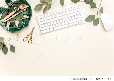 Flat lay home office desk. Female workspace with computer, plate sheet monstera, golden accessories, eucalyptus leaves, on beige background. Top view Flat lay home office desk. Female workspace with computer, plate sheet monstera, golden accessories, eucalyptus leaves, on beige background. Top view 69154238
