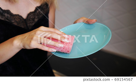 Blue plate with pink dish sponge in hand on blurred background 69154567