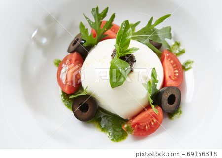 Traditional authentic soft and creamy fresh Italian burrata cheese shaped as white round ball over Italian tomatoes topped with rucola along side pesto reduction Traditional authentic soft and creamy fresh Italian burrata cheese shaped as white round ball over Italian tomatoes topped with rucola along side pesto reduction 69156318