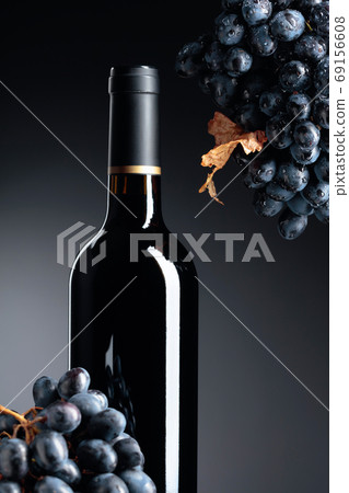 Unopened bottle of red wine and dark blue grapes with dried leaf 69156608