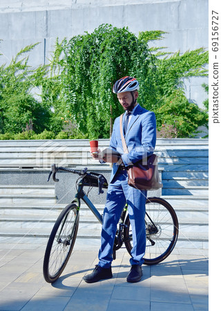 Businessman with bicycle holding coffee cup and digital tablet. 69156727