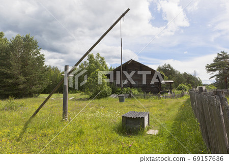 Water well on the background of an old house with boarded up windows. Russian remote Water well on the background of an old house with boarded up windows. Russian remote 69157686