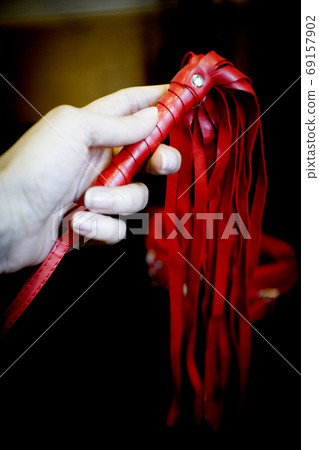 Womans hand holding handcuffs and whip for sex games 69157902