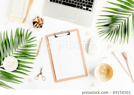 Flat lay home office desk. Female workspace with computer, clipboard, tropical palm leaves, accessories on white background. Top view. Flat lay home office desk. Female workspace with computer, clipboard, tropical palm leaves, accessories on white background. Top view. 69158501