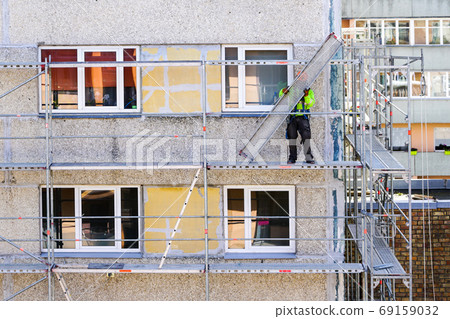 the worker assembles the scaffolding on the facade of a multi-storey house at a dangerous height the worker assembles the scaffolding on the facade of a multi-storey house at a dangerous height 69159032