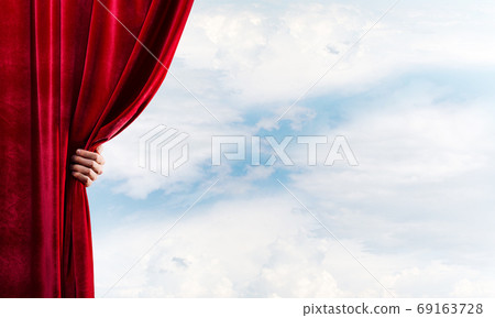 Cloudy landscape behind red curtain and hand holding it 69163728